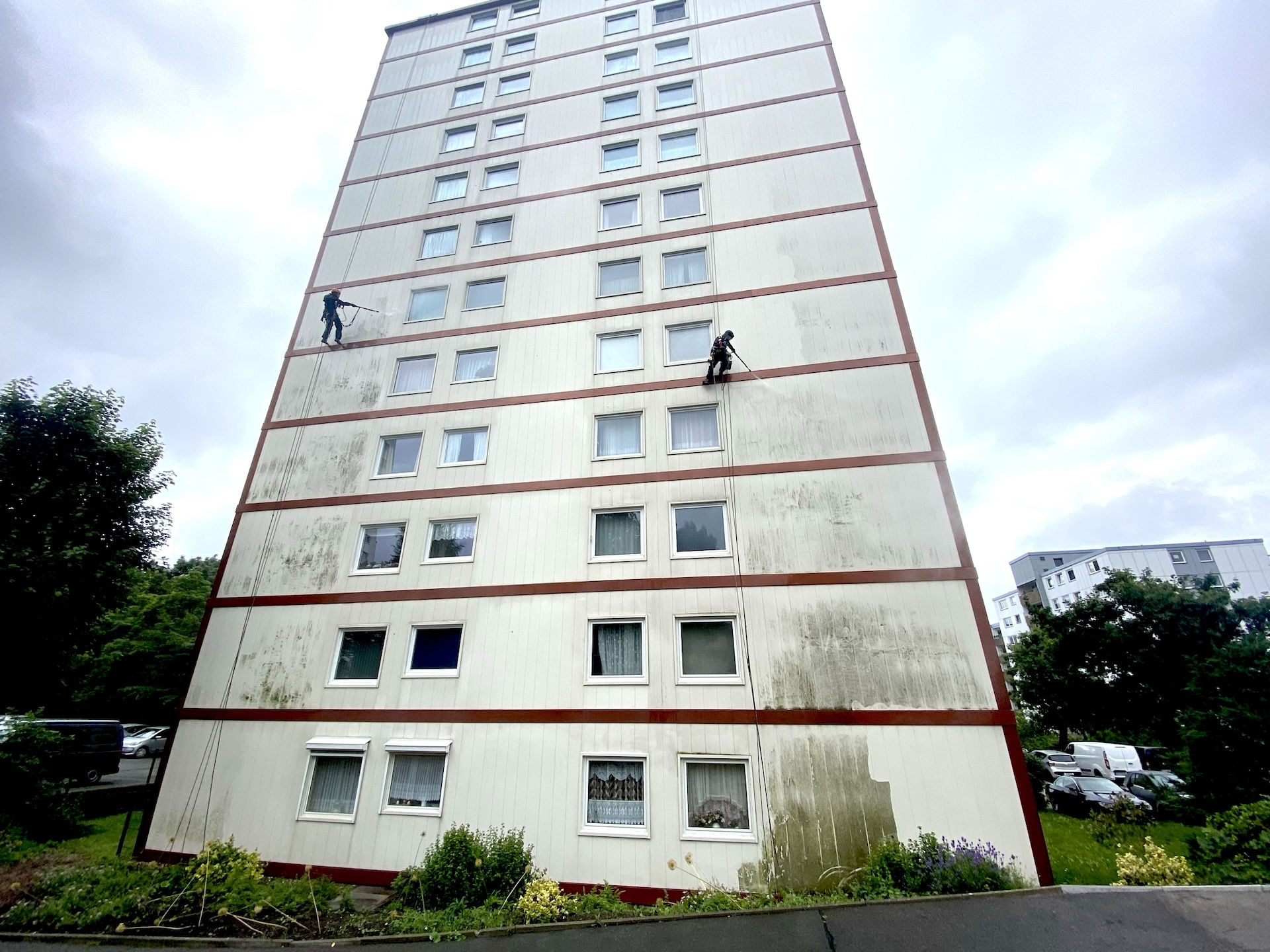 Zwei Industriekletterer reinigen die Fassade eines zwölfstöckigen Hochhauses mit Hochdruckreinigern.