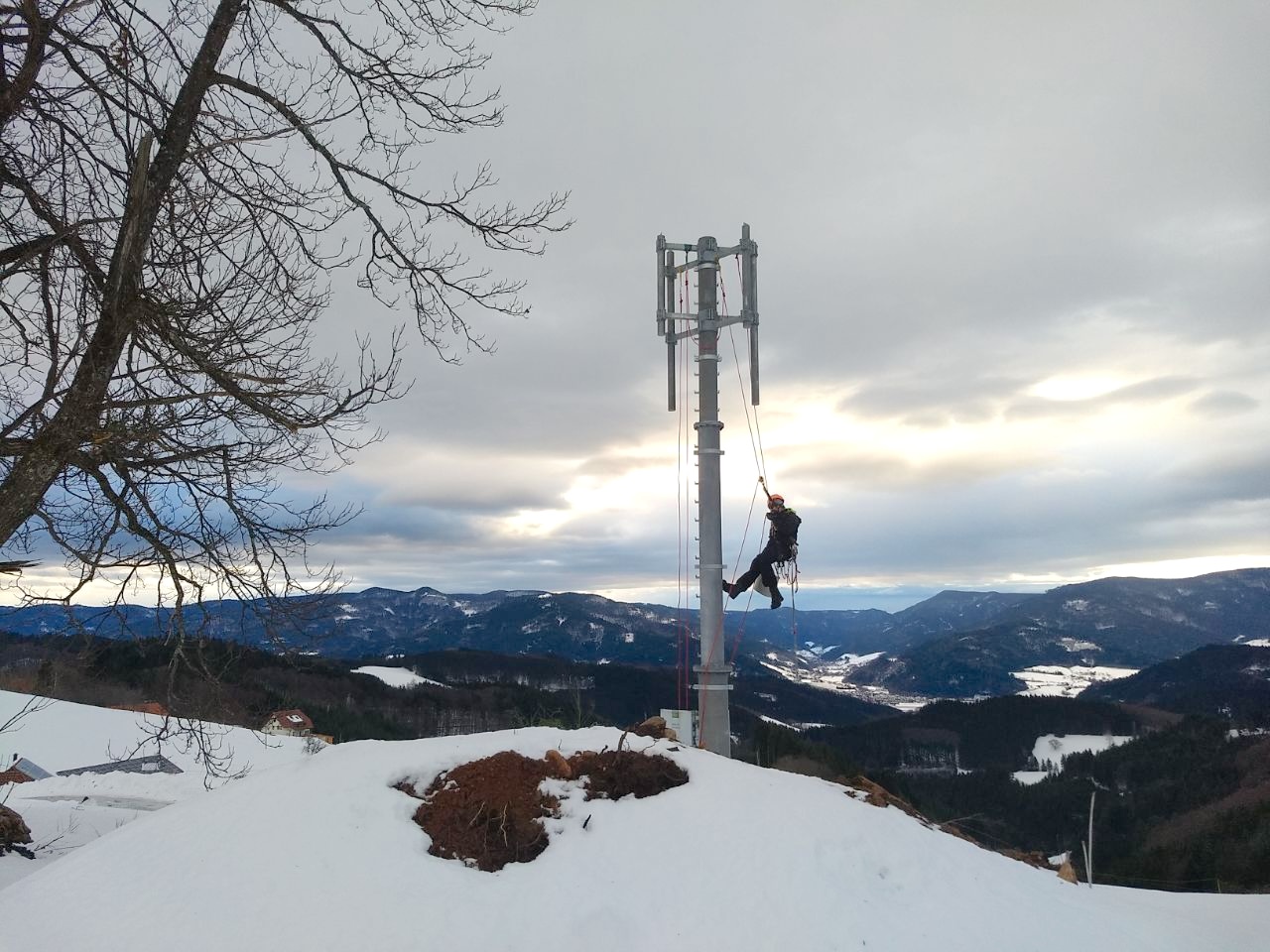 Ein Kletterer hängt an einem Mobilfunkmast inmitten einer verschneiten Gebirgslandschaft